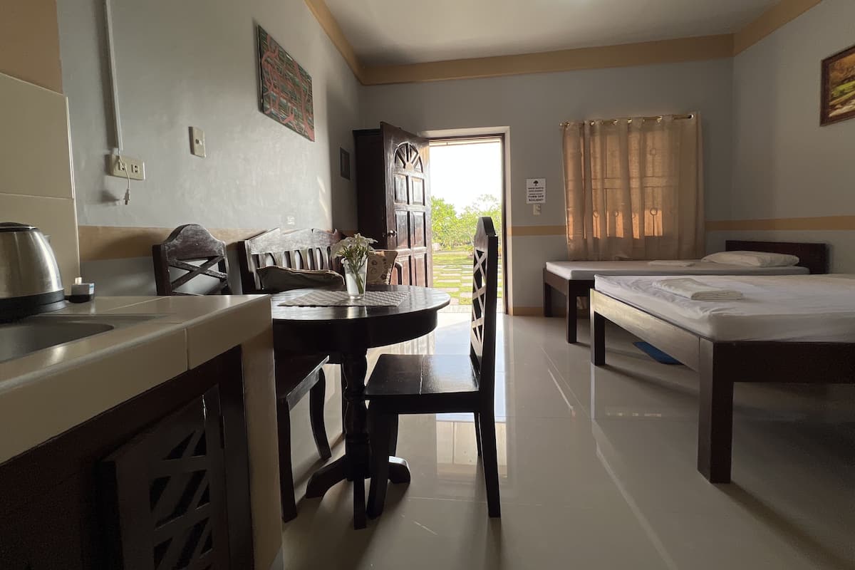 A hotel room with a dining table, chairs, a bed, a window with curtains, and a view of the outdoors.