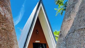 Un edificio moderno de forma triangular con techo plano, rodeado de árboles grandes y una zona verde.