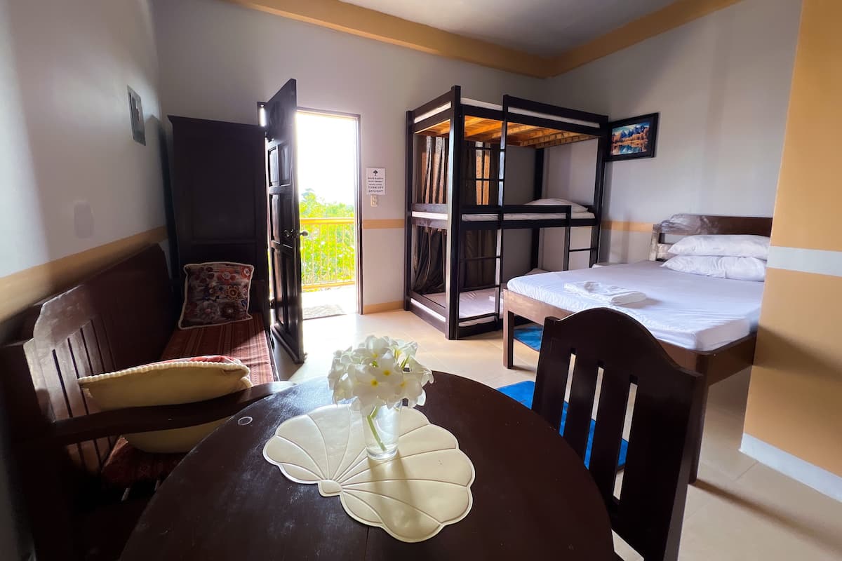 A room with a bunk bed, a dining table with a vase of flowers, a chair, and a bench.