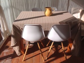 A table with a beige tablecloth, two white chairs, and a yellow pitcher.