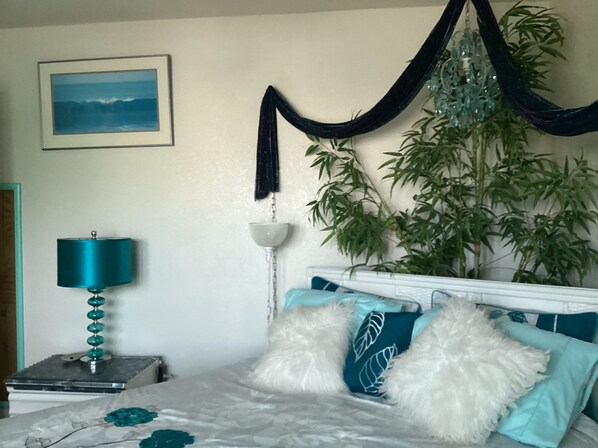 Une chambre à coucher avec un lit, une table de chevet, une lampe, une plante suspendue et un tableau encadré au mur.