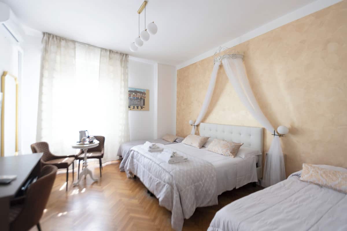 Ein Hotelzimmer mit zwei Betten, einem Essbereich und einem großen Fenster mit Vorhängen.