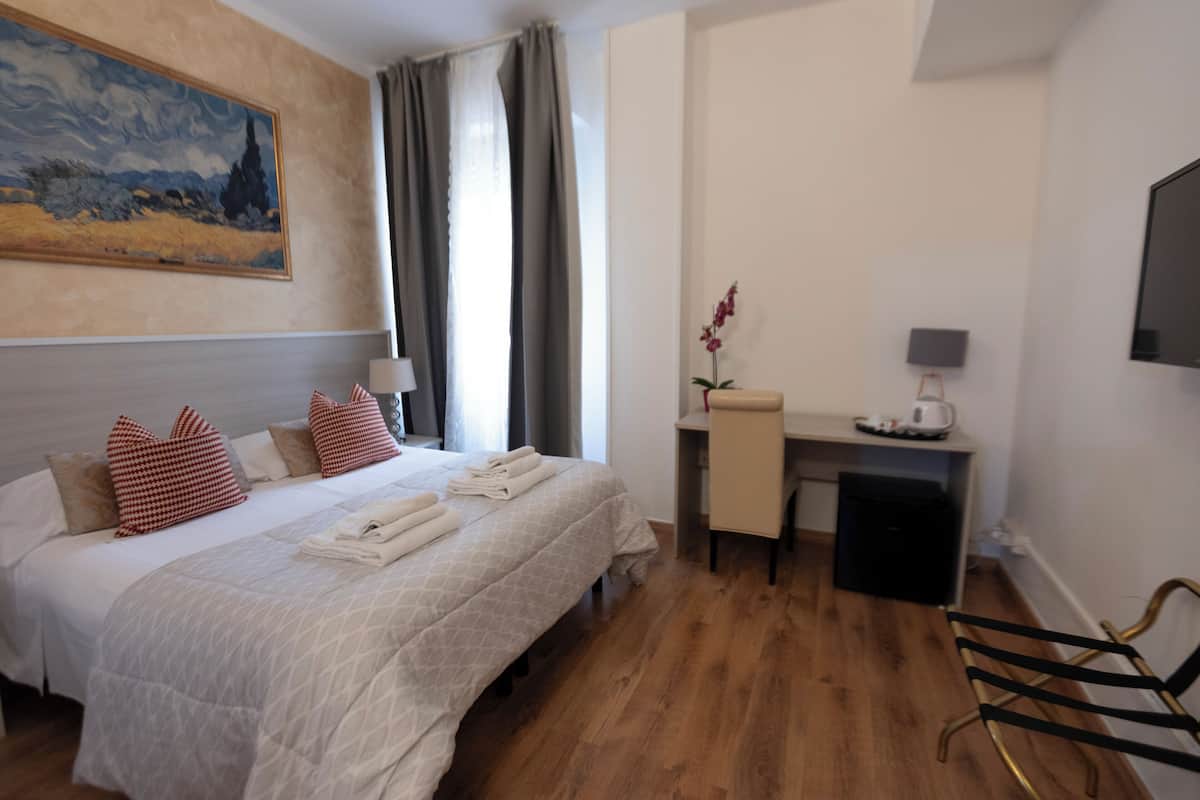 Ein Hotelzimmer mit Bett, Schreibtisch, Stuhl, Fernseher und einem Bild an der Wand.