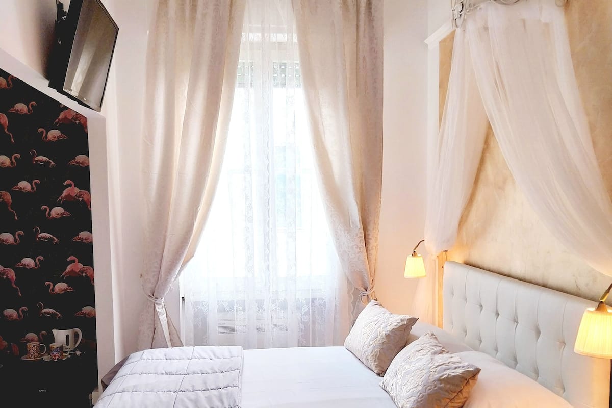 Ein Schlafzimmer mit einem großen Bett, einem Kopfteil mit heller, gepolsterter Struktur und transparenten Vorhängen.