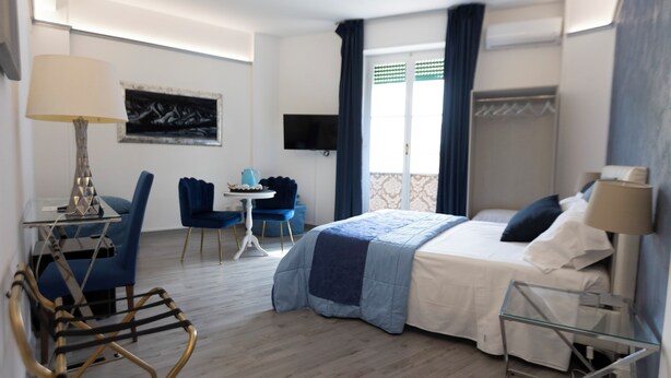 A hotel room with a bed, a desk, a chair, a TV, and a balcony with curtains. - Soggiorno La Coccinella (Florence)
