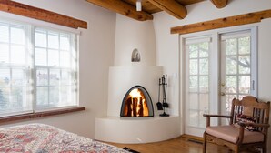 A cozy room with a fireplace, wooden beams, a patterned rug, and a chair. - Light Filled, Spacious Casita~Walk to Downtown & Mountain Views (Santa Fe)