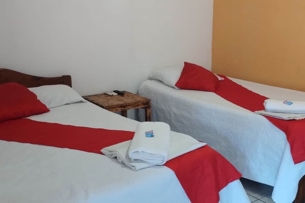 Two single beds with red and white bedding, a wooden nightstand, and a small table with a towel.