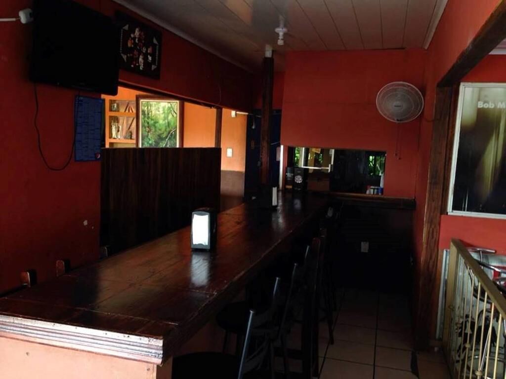 Een bar met een houten toonbank, stoelen, een ventilator en een raam met uitzicht.