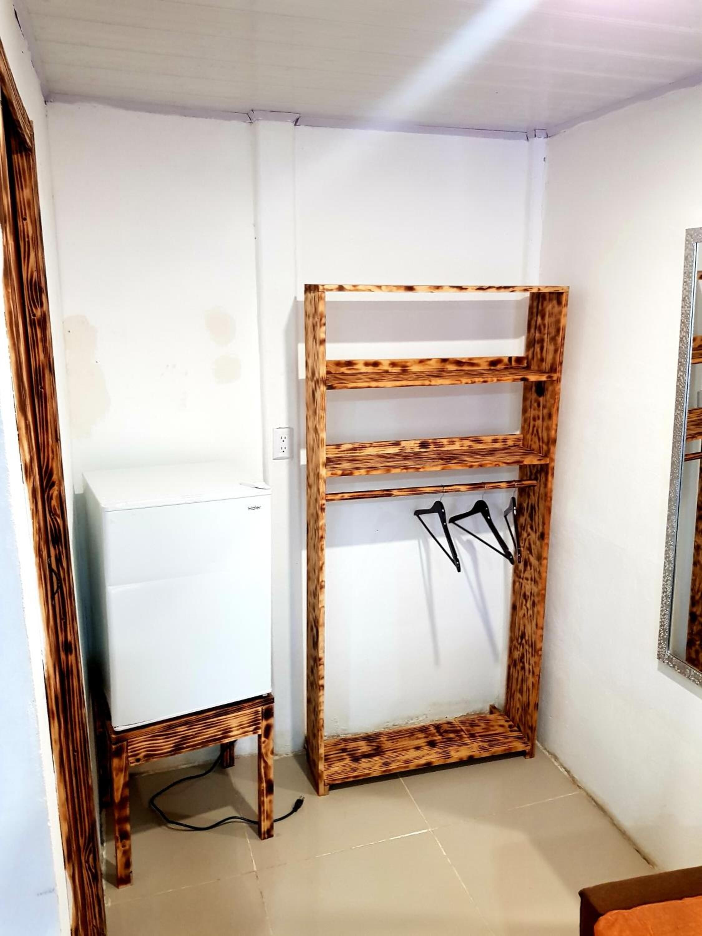 A compact room with a white wall, a wooden cabinet with shelves, and a mirror.