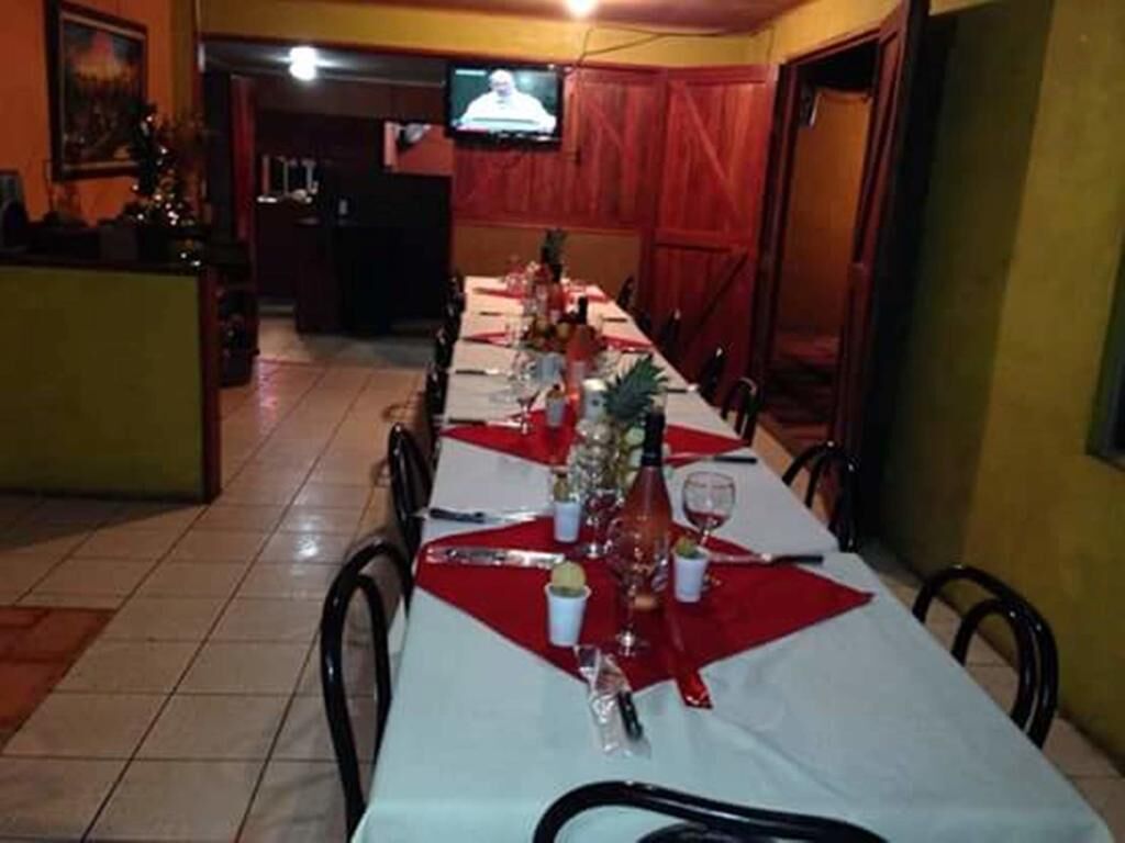 A dining area with a long table set for a meal, chairs around it, and a television mounted on the wall.