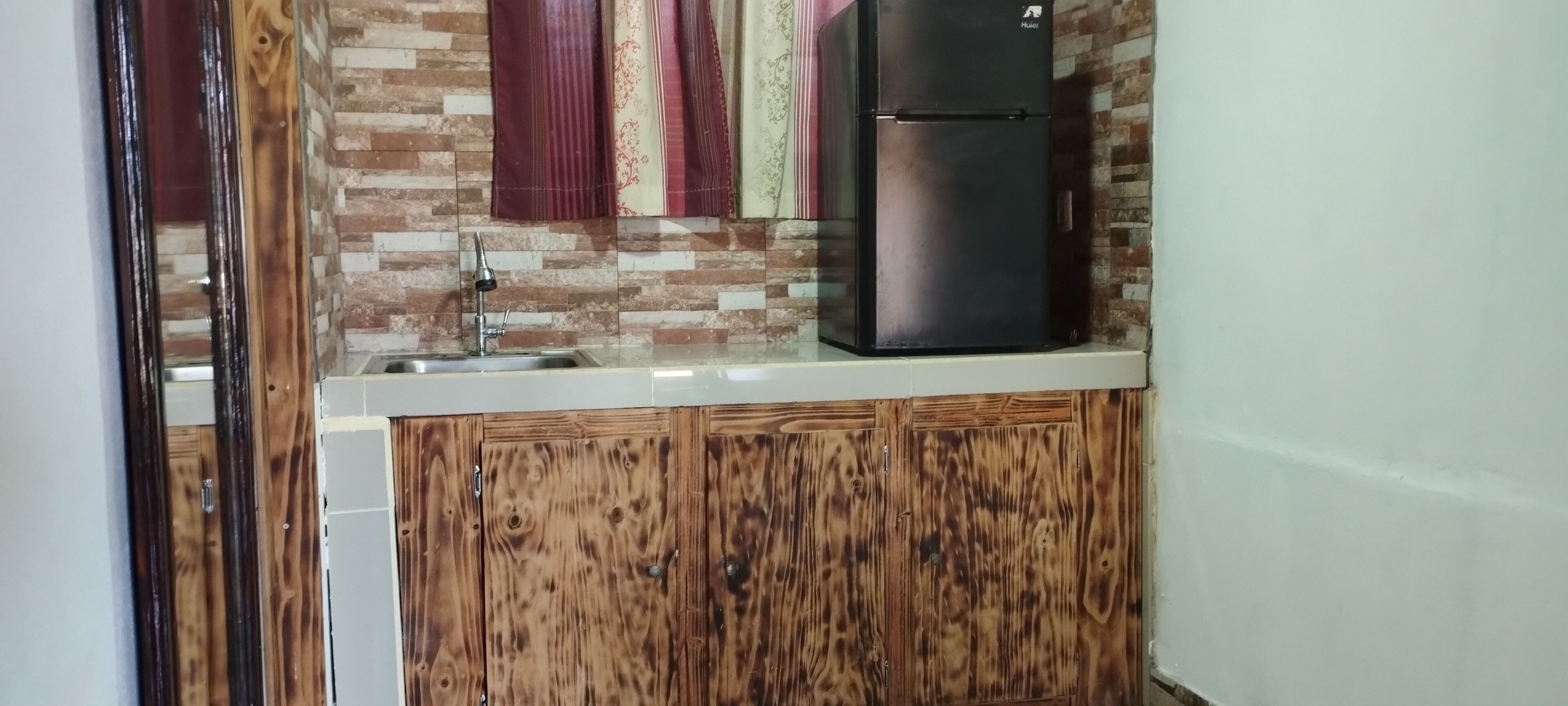 A kitchen with a sink, a black refrigerator, wooden cabinets, and a tiled backsplash.