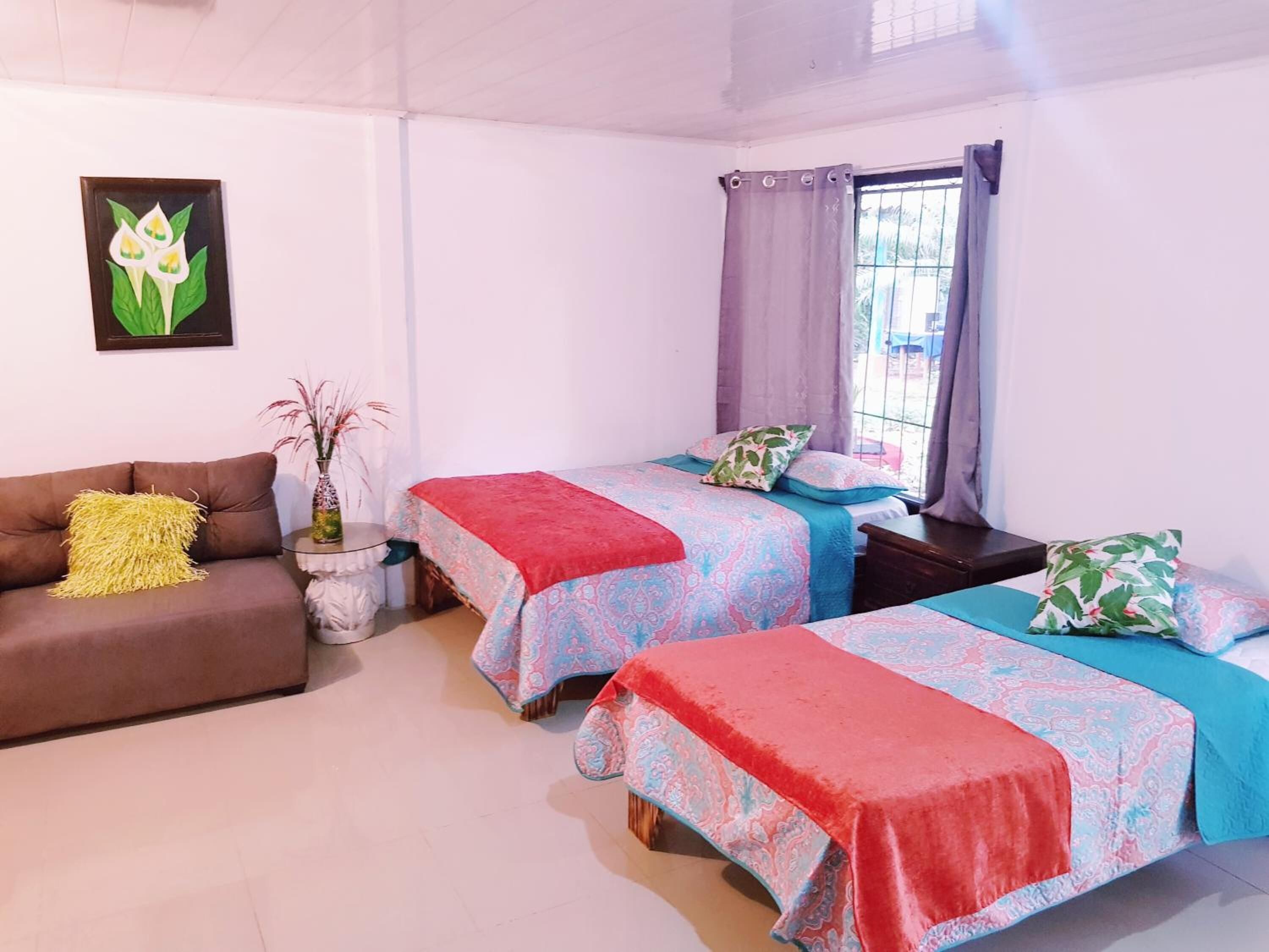 A bedroom with two single beds, a sofa, a small table, and a window with curtains.