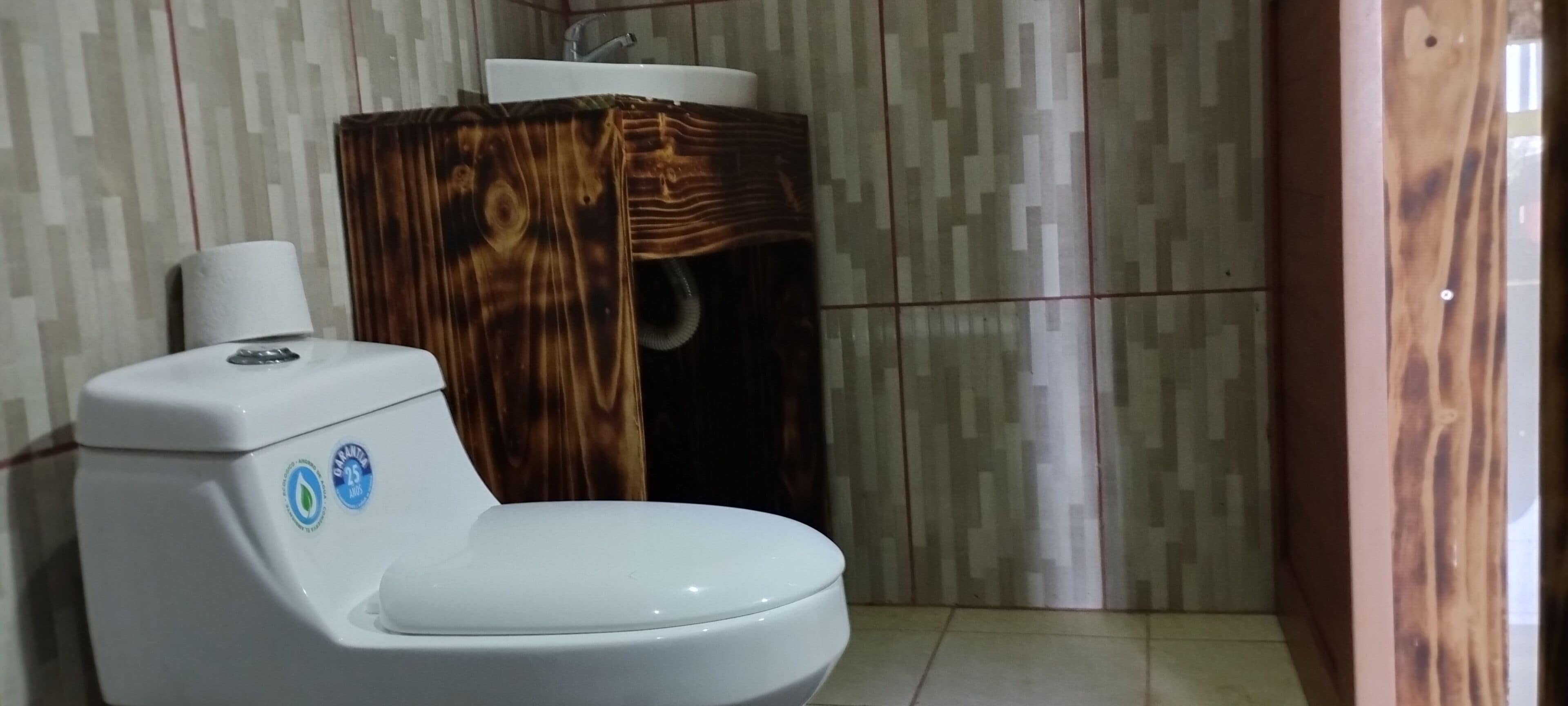 Un baño con un inodoro blanco, un tocador de madera y un papel tapiz estampado.