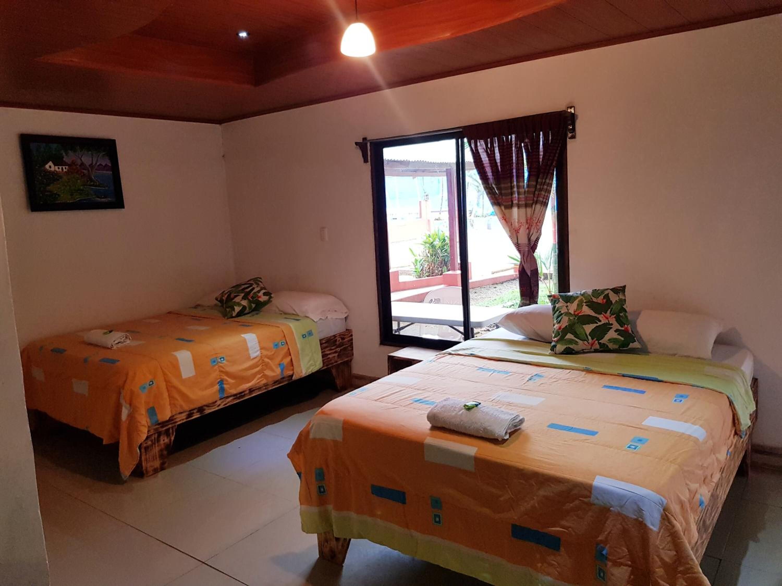 Una habitación con dos camas, una ventana con cortinas, un cuadro en la pared y una lámpara en el techo.