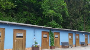 Fileira de quartos azuis com portas e janelas de madeira, cada um com um pequeno vaso de plantas e um banco na parte externa.