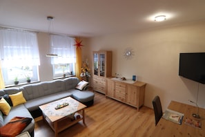 Una sala de estar con sofá, reposapiés, mueble de madera y televisor de pantalla plana.