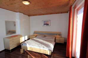 Une chambre avec un plafond en bois, un lit recouvert d’une couvre-lit à rayures beige et blanches, une commode, une table de chevet et un tableau encadré accroché au mur.