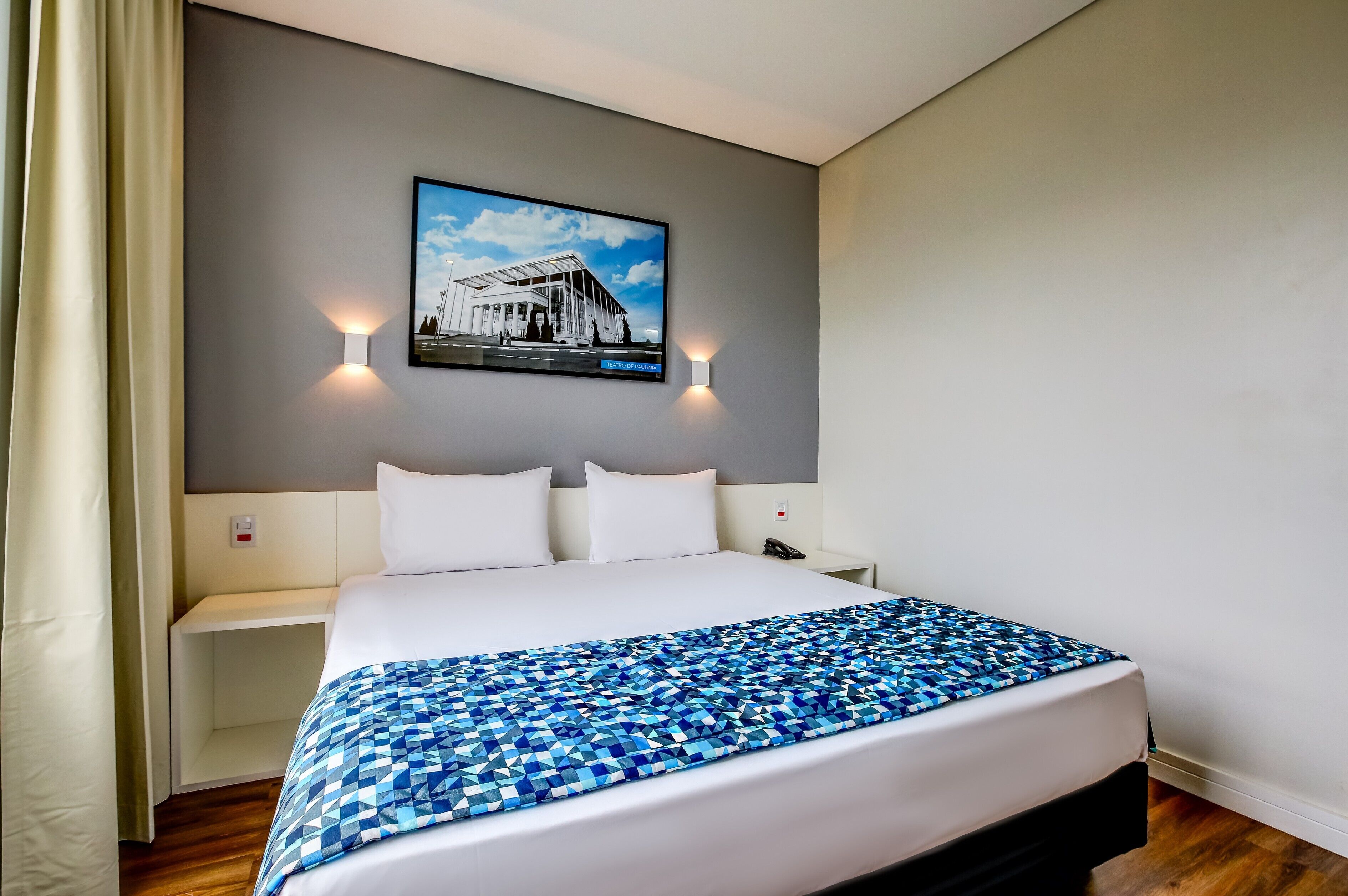 Une chambre d’hôtel avec un grand lit, une table de chevet, un téléviseur fixé au mur et deux appliques murales.
