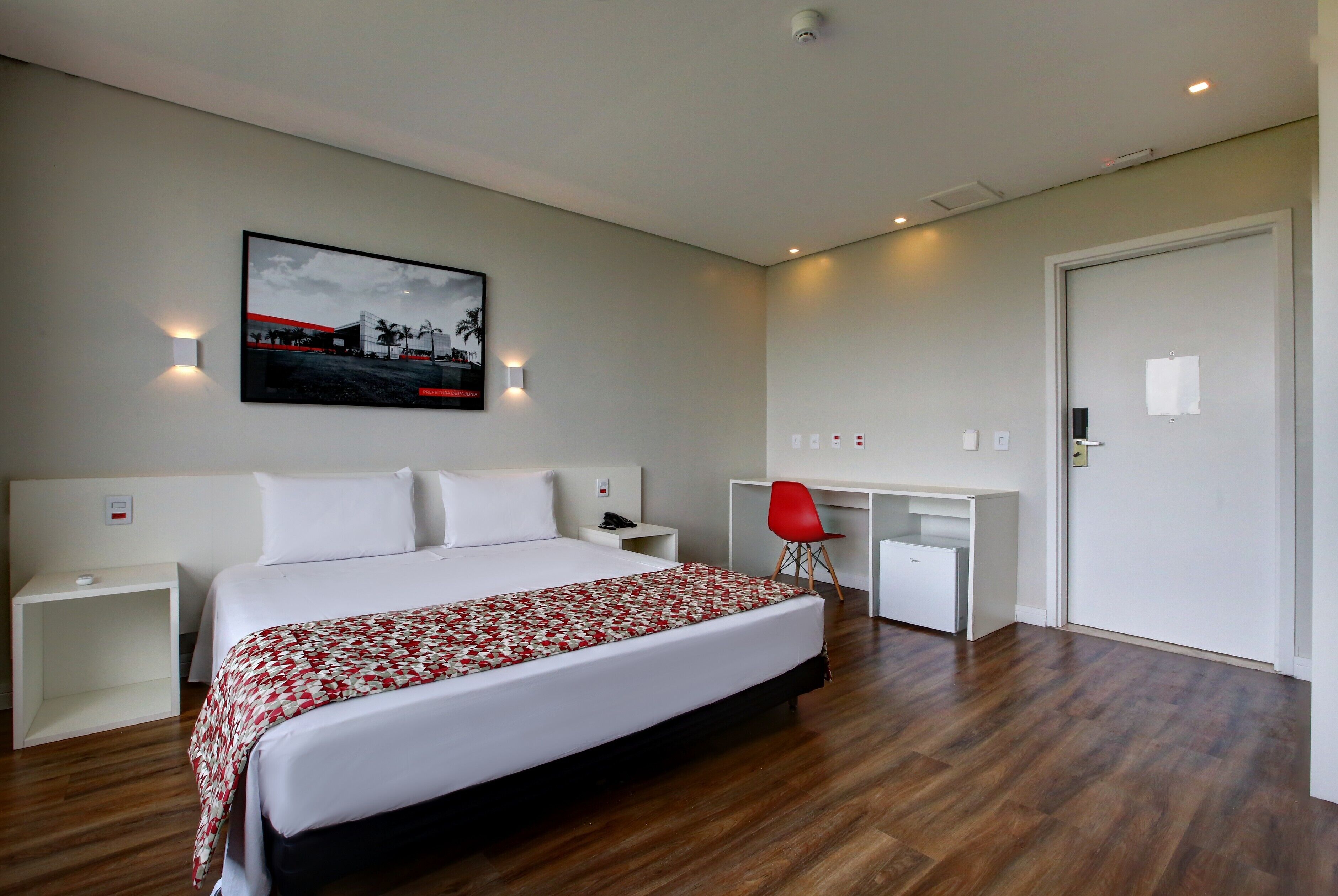 Et moderne hotelværelse med en stor seng, et skrivebord og en rød stol.
