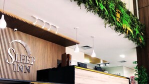 A reception desk with a wooden finish and a sign that reads "Sleep Inn." There are hanging pendant lights above the desk, and a green plant decoration is visible in the background. - Sleep Inn Paulinia (Paulinia)