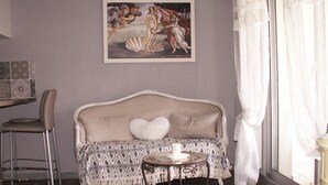 Una sala de estar con un sofá, una mesita redonda pequeña, una silla y un cuadro en la pared.