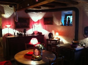 A dimly lit room with a round wooden table, a lamp, and a window with a view.