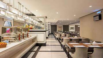 Un comedor moderno de hotel con mostradores tipo buffet, mesas largas y sillas.