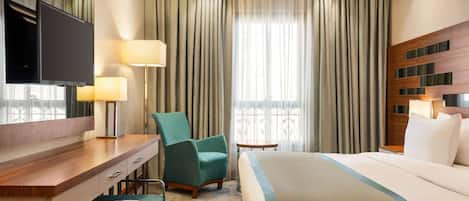 A hotel room with a bed, a desk, a chair, a TV, and a window with curtains.