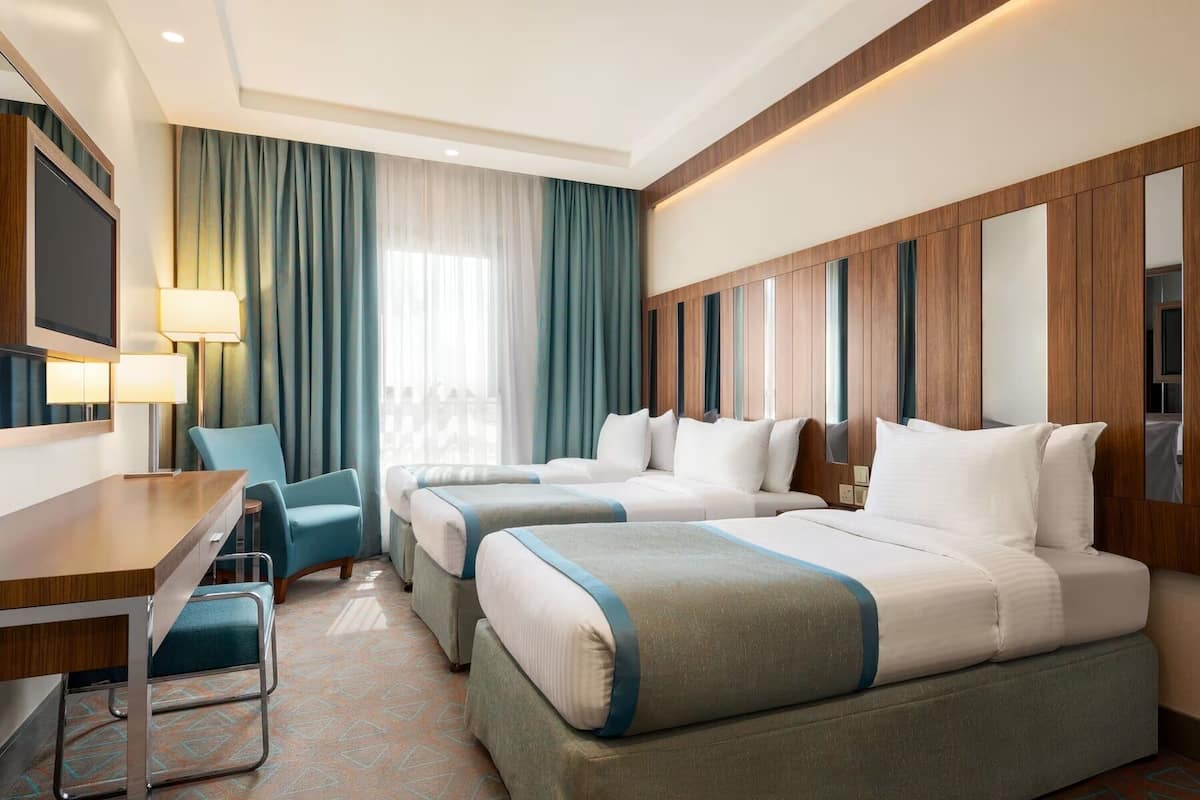 Habitación de hotel con dos camas, un escritorio, una silla, un televisor y una ventana con cortinas.