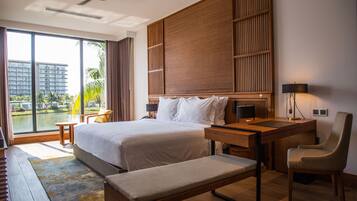 Ein modernes Hotelzimmer mit einem großen Bett, einem Schreibtisch, einem Stuhl, einer Bank und Blick auf ein Gewässer sowie Gebäude.
