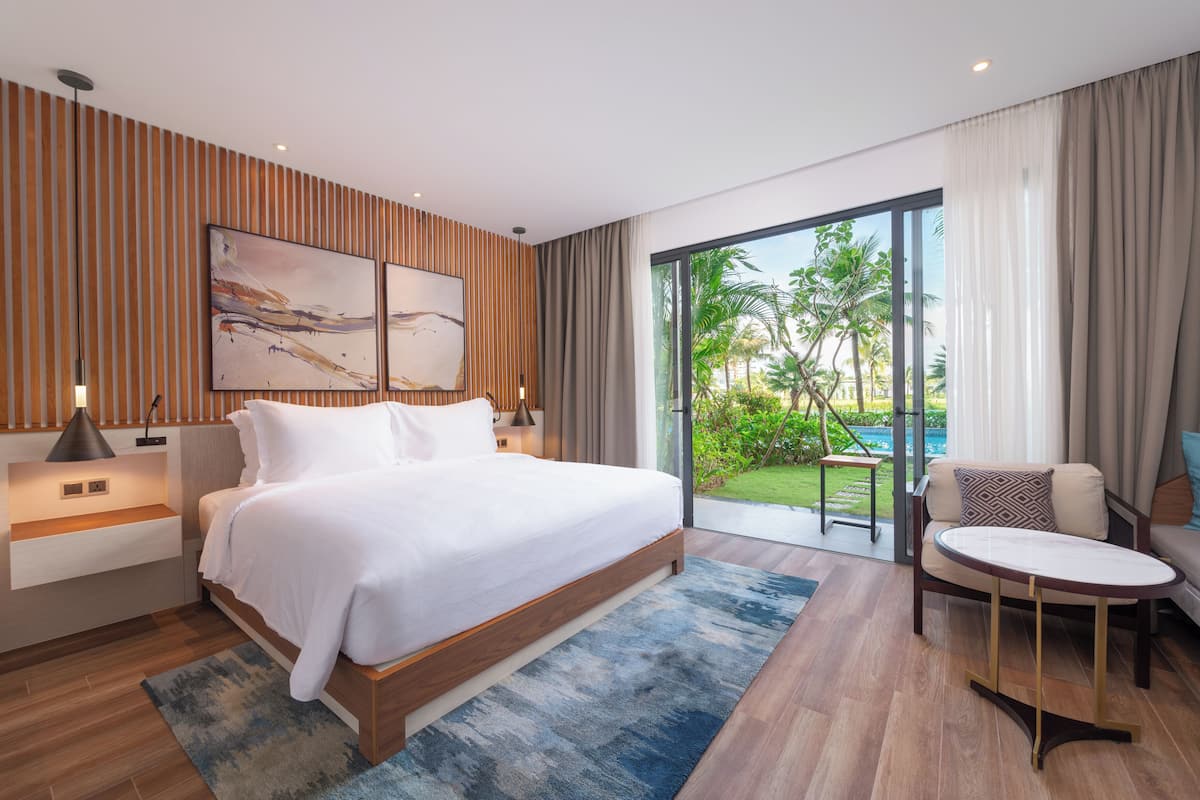 Ein modernes Schlafzimmer mit einem großen Bett, einer Couch und Blick auf Garten und Pool.
