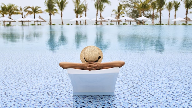 A person relaxing in a pool with a view of palm trees and umbrellas. - Mövenpick Villas & Residences  Phu Quoc (Phu Quoc)