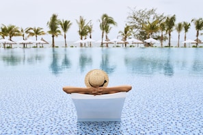 A person relaxing in a pool with a view of palm trees and umbrellas. - Mövenpick Villas & Residences  Phu Quoc (Phu Quoc)