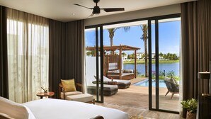 A hotel room with a bed, a ceiling fan, a view of a pool and palm trees, and a wooden deck. - Mövenpick Villas & Residences  Phu Quoc (Phu Quoc)