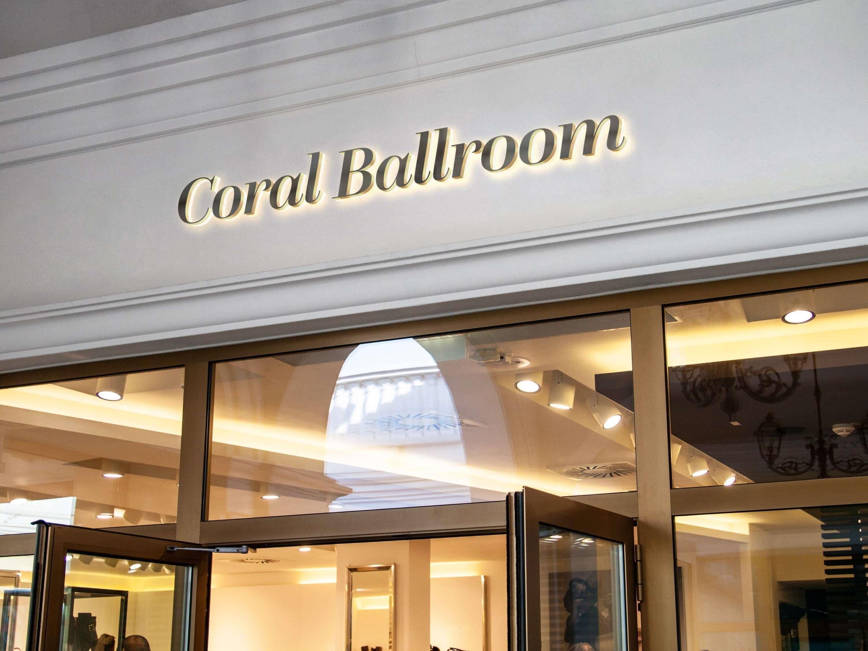 A sign for 'Coral Ballroom' with a modern interior design, glass doors, and ceiling lights.