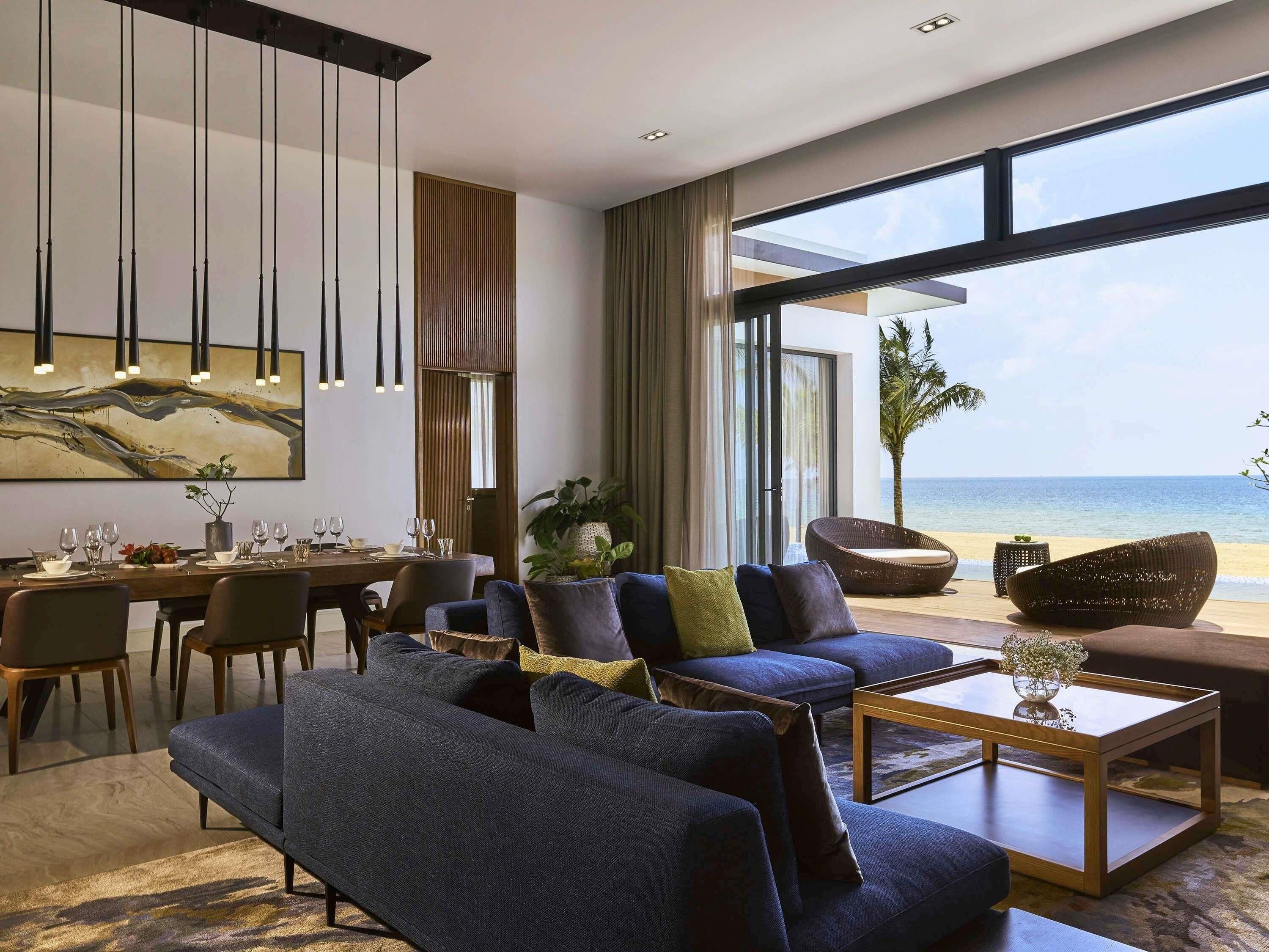 A modern living room with a large window overlooking the sea, a dining area with a table set for four, and a comfortable seating arrangement.