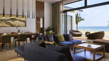A modern living room with a large window overlooking the sea, a dining area with a table set for four, and a comfortable seating arrangement.