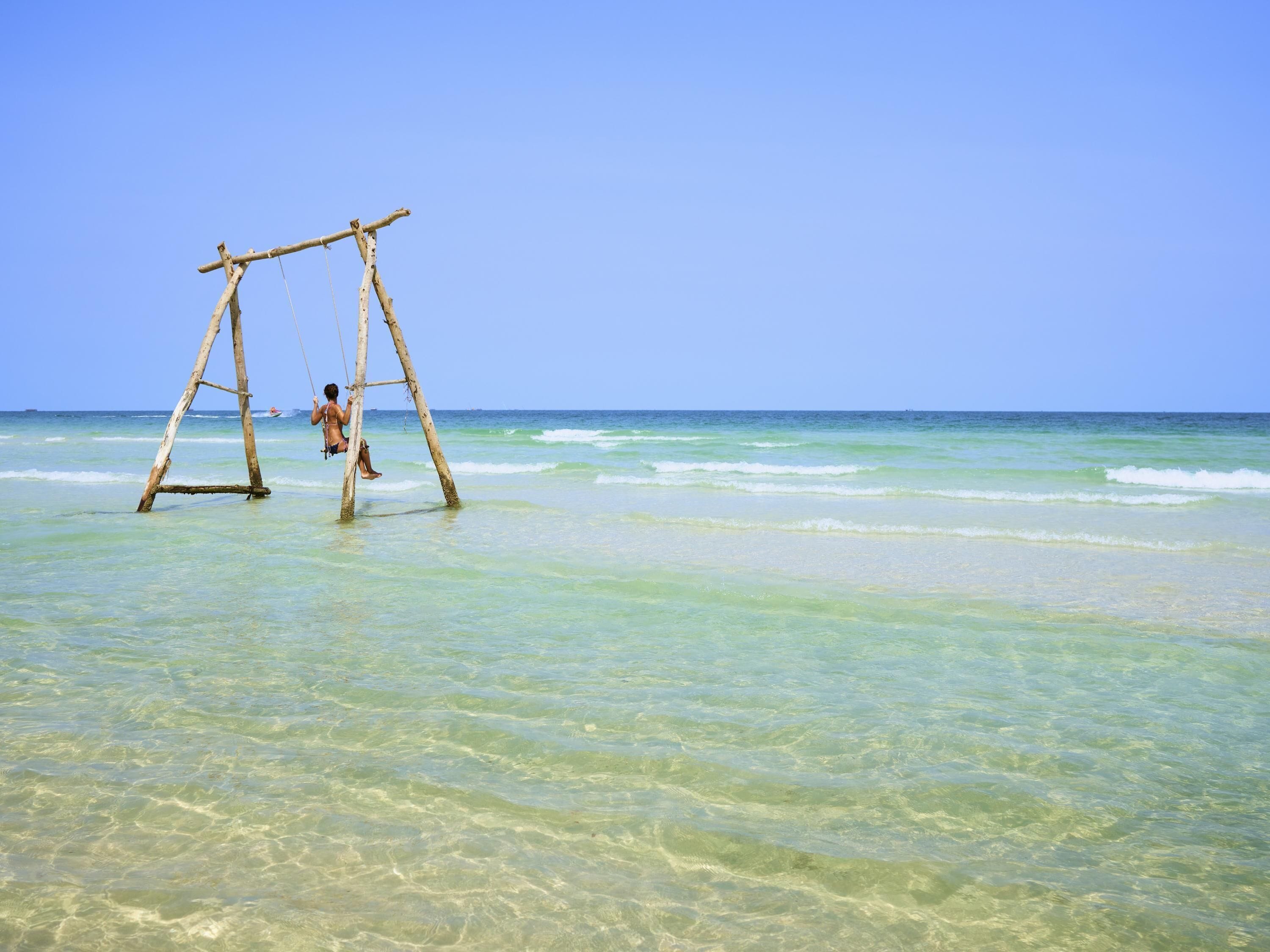 A beach with clear water and a wooden swing set.
