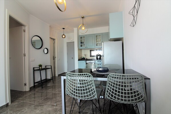 A modern kitchen with a dining area, featuring a black countertop, two chairs, and a round table. - Appart. 4 pers. Large terrace with sea view. 500m from the historic center (Albufeira)