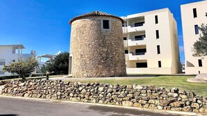 Une tour en pierre, surmontée d’un toit plat, entourée d’un mur de pierre et d’une zone herbeuse.