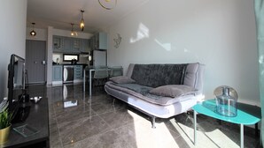Un salon moderne avec un canapé gris, une table basse en verre et un téléviseur posé sur un meuble.