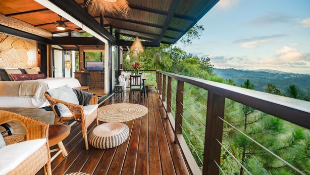Una terraza de madera con mobiliario de mimbre, un televisor y vistas a las montañas.