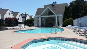 Una piscina con sillones de descanso y una zona cubierta, rodeada de casas.