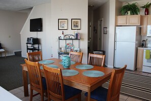A dining area with a wooden table and chairs, a television mounted on the wall, and a kitchen area with a refrigerator and cabinets. - AMAZING! 4Bed/3Bath Water's Edge Beach House with Pool and Hot Tub! (Port Clinton)