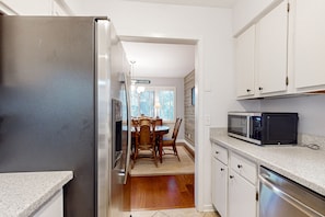 Compact kitchen with modern appliances, dining area, and wooden table.