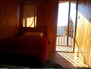 Une chambre dans un chalet en bois, avec un lit, une fenêtre avec des rideaux et un balcon donnant sur un immeuble.
