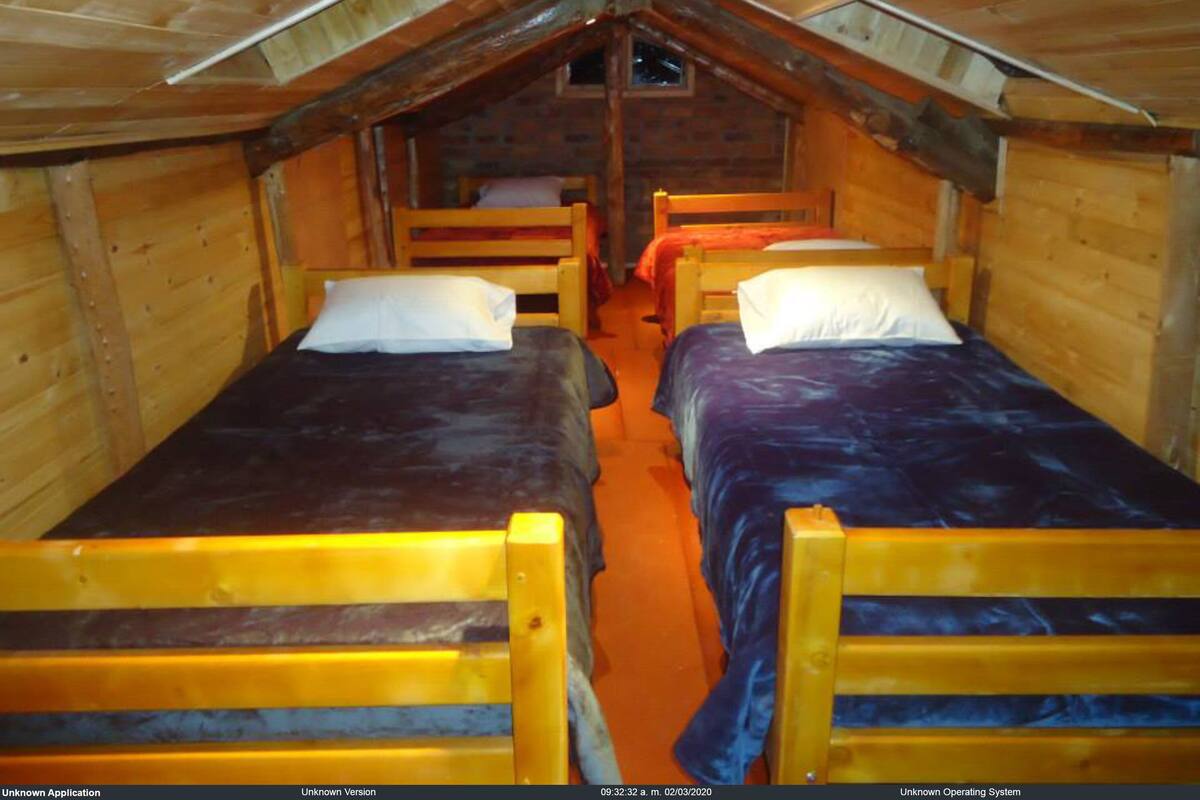 Een klein, rustiek huisje met twee houten bedden, elk voorzien van een kussen en een deken.