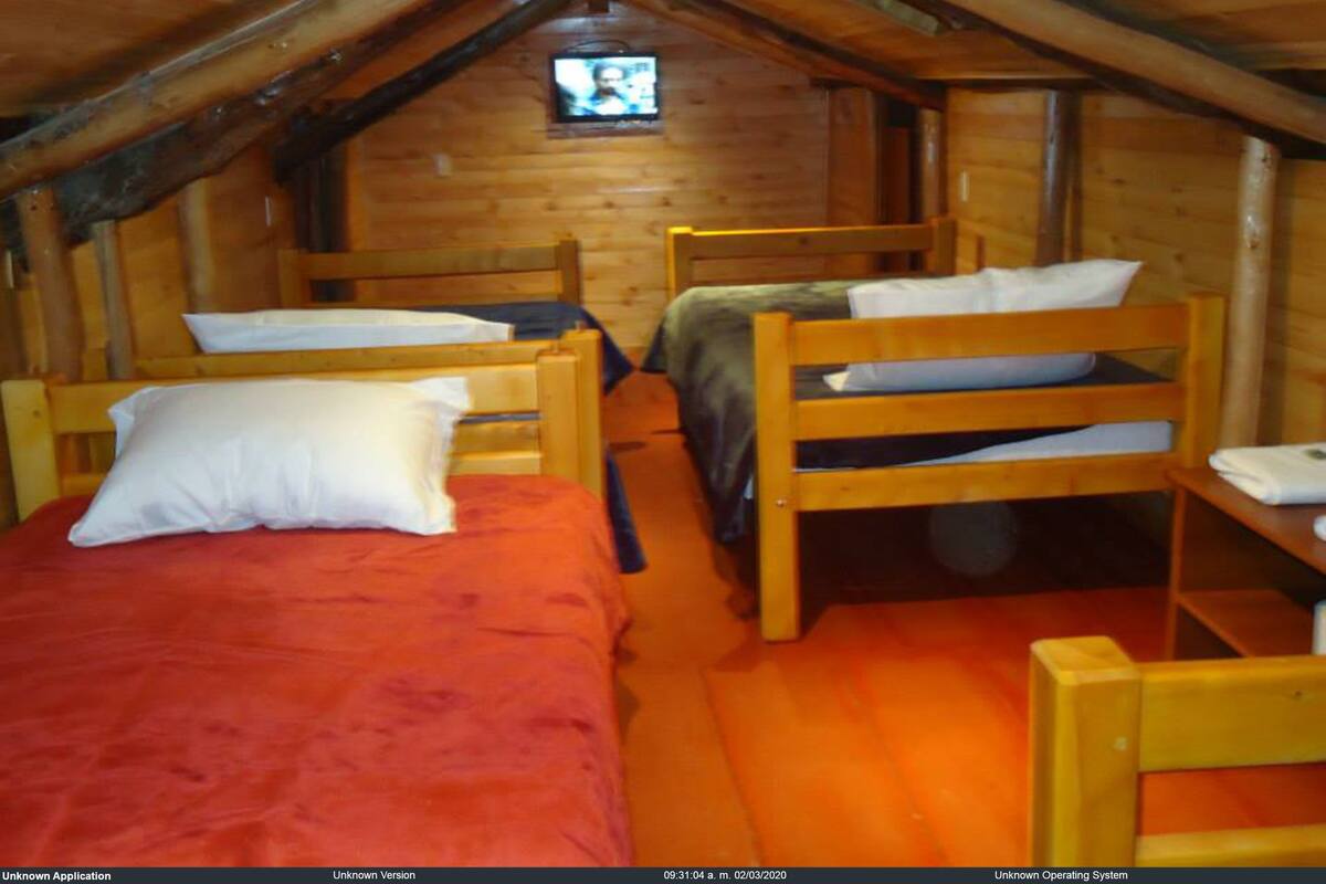 Een knus zolderkamer met houten wanden en schuine plafonds, met daarin drie houten stapelbedden met kussens en dekens.