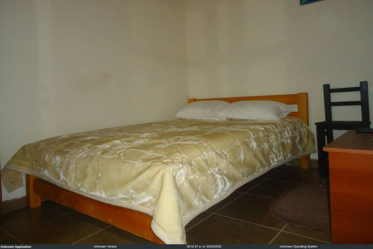 Een enkel bed met houten frame en een beige sprei in een kamer met gladde muren en een betegelde vloer.