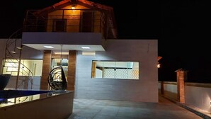 Uma casa moderna de dois andares com varanda, cadeira suspensa e uma pequena janela.